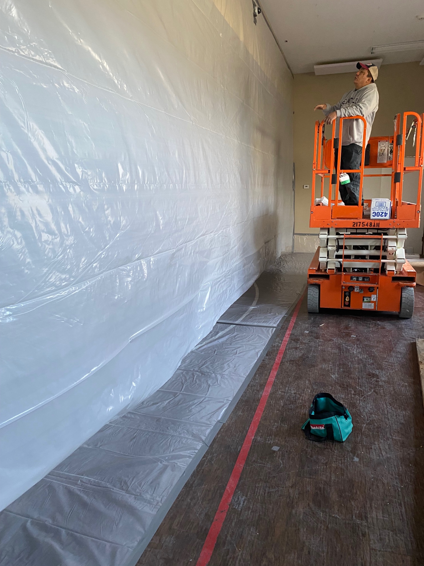 Prime Environmental Solutions specialist on a scissor lift installing full poly containment for asbestos abatement